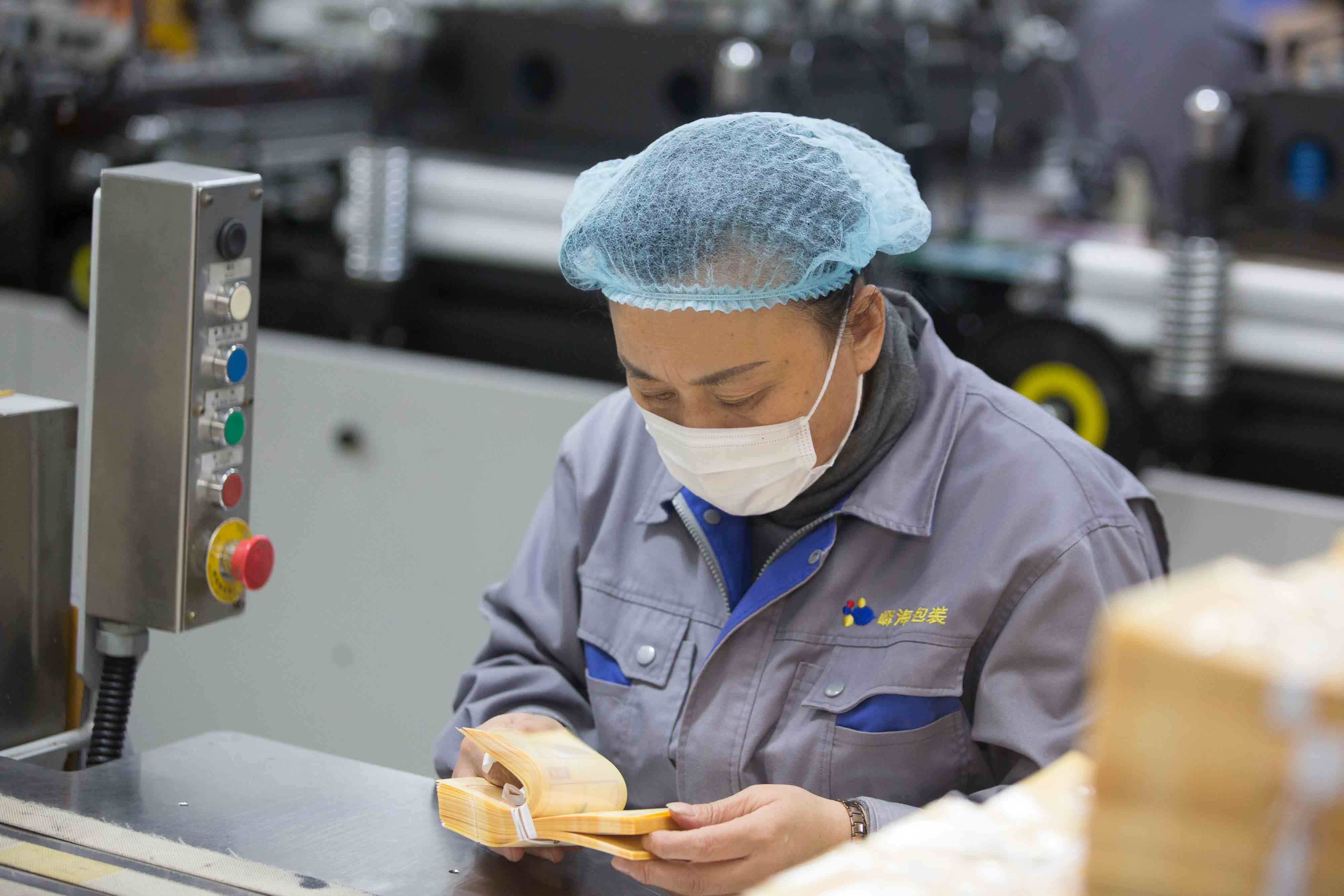 An operator handling packaging pouches beside factory equipment