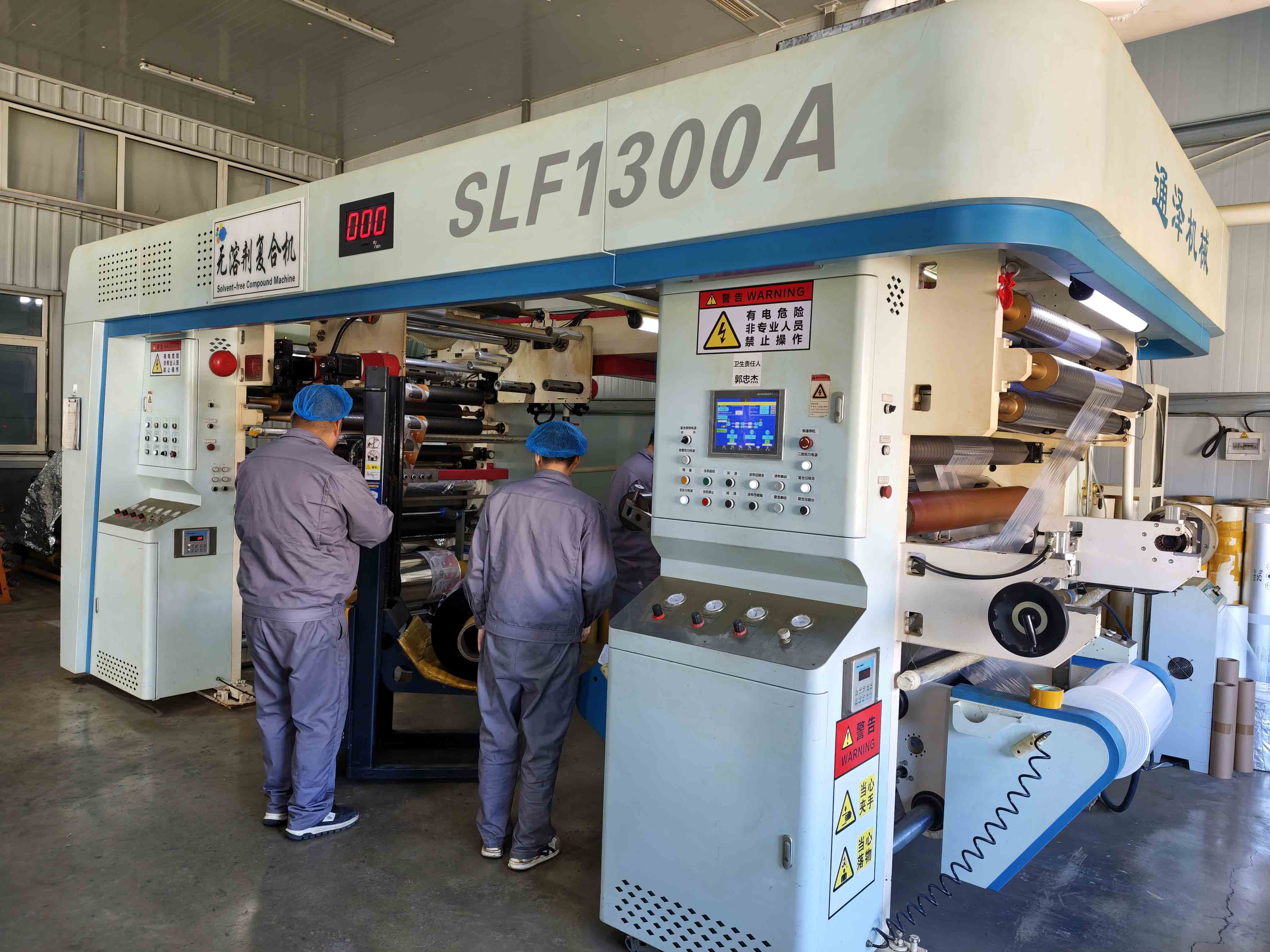 Two operators beside lamination equipment in the packaging factory